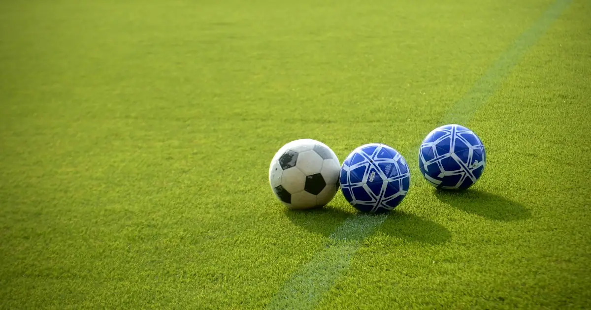 Three footballs lined up on a training pitch