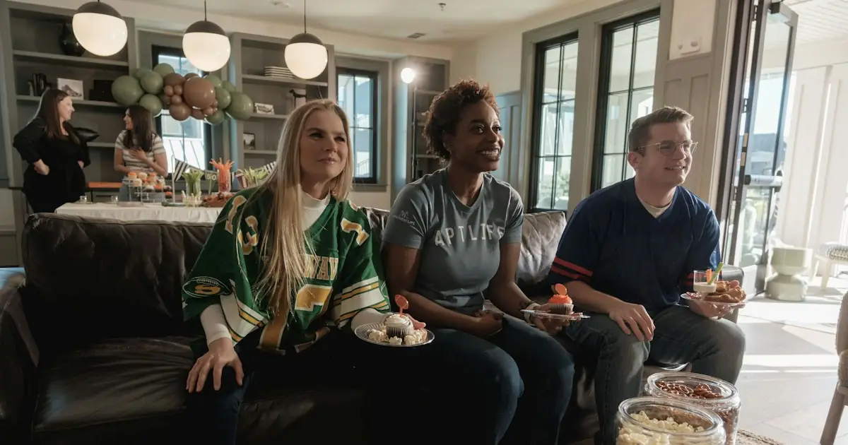 Three friends in football shirts sharing snacks on a sofa during a game