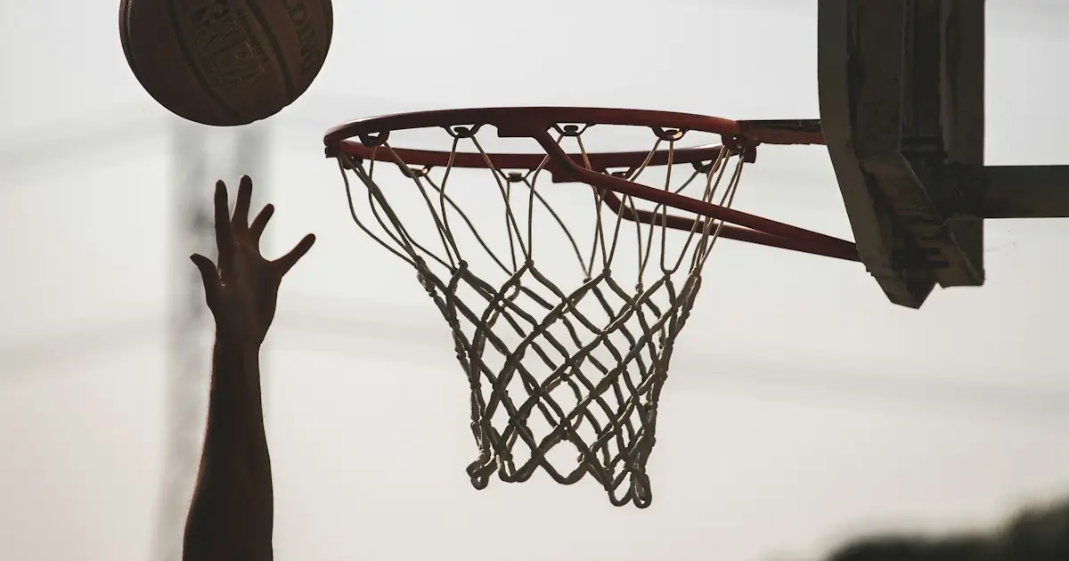 A hand reaching up as a basketball flies towards the hoop